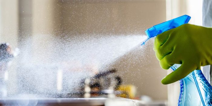disinfecting a home using a spray bottle and rubber gloves