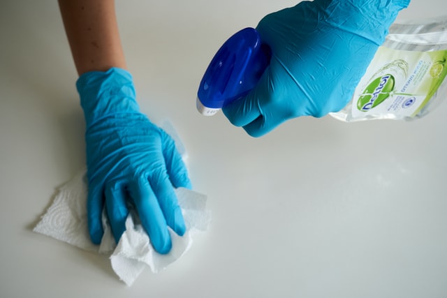 sanitizing a surface with a spray bottle and rubber gloves