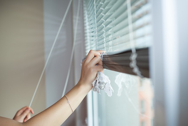 Woman cleaning mini blinds in a bedroom