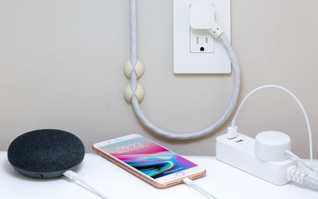 a white cell phone plugged in and charging next to a small black speaker